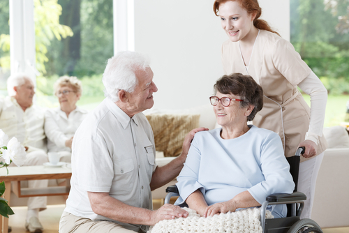 Senior man and woman smiling and sitting in wheelchair while at a assisted living facility