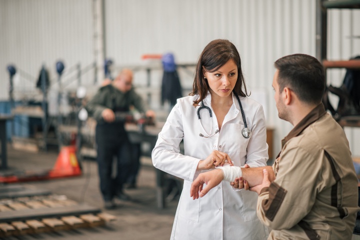 Doctor bandaging arm of a injured factory worker